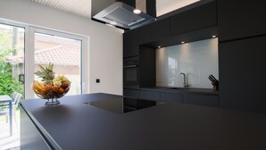 A modern kitchen with a large island, built-in oven, and a bowl of fruit on the counter.