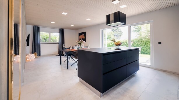 A modern kitchen with a large island, recessed ceiling lights, and a view of greenery outside.