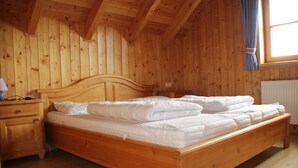 Una habitación de madera con una cama, una mesita de noche y un ventanal con cortinas.