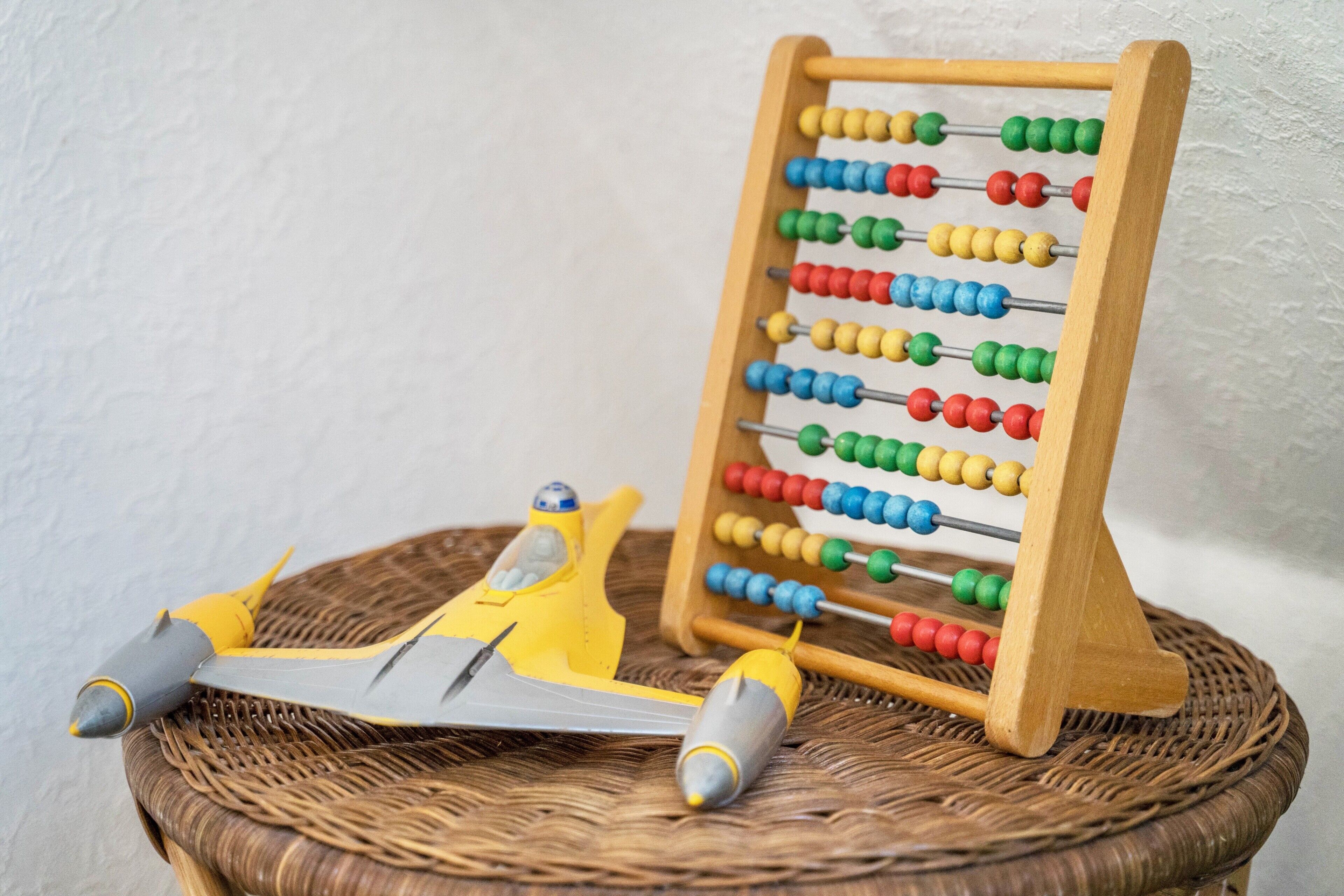 Un ábaco de madera con cuentas de colores, un avión de juguete amarillo y una cesta de mimbre.