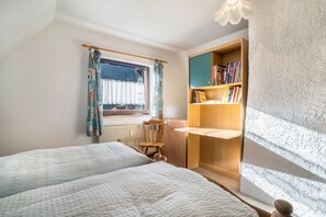Une chambre avec deux lits, une fenêtre avec des rideaux, une bibliothèque et un radiateur.