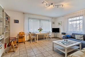 Un salon comprenant un canapé, une table basse, un téléviseur, une bibliothèque et une fenêtre avec des rideaux.