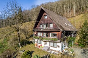 Une maison en bois dotée d’un balcon, entourée d’arbres et d’une zone herbeuse.