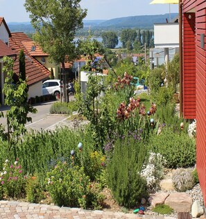 Et boligområde med en asfalteret indkørsel, parkerede biler og mange blomstrende planter.