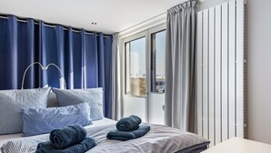 A hotel room with a bed, pillows, a window, curtains, and a view of the city.