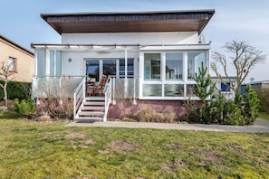 Une maison moderne à deux étages, dotée d’un porche abrité, d’un escalier et offrant une vue sur le paysage environnant.