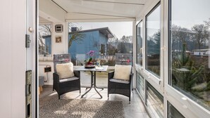 A modern patio with a table and two chairs, a view of the neighborhood, and a large window.
