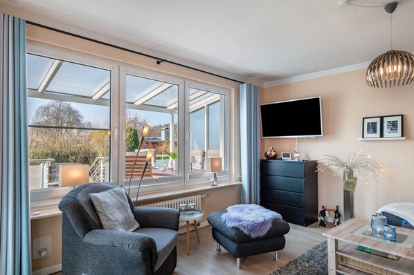 Un salon moderne avec un canapé, un pouf et un téléviseur fixé au mur.