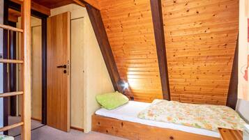 A bedroom with a sloped ceiling, wooden beams, a bed with a floral bedspread, a green pillow, and a wooden nightstand.