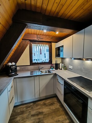 A modern kitchen with a built-in oven, a coffee machine, and a window with curtains.