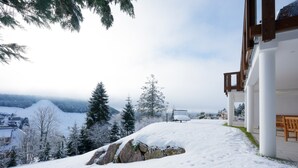 Schneebedeckte Landschaft mit einem Gebäude, das einen Balkon und einen Blick auf eine Stadt im Hintergrund bietet.