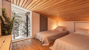 A cozy bedroom with two beds, wooden ceiling, and a large window overlooking a snowy forest.