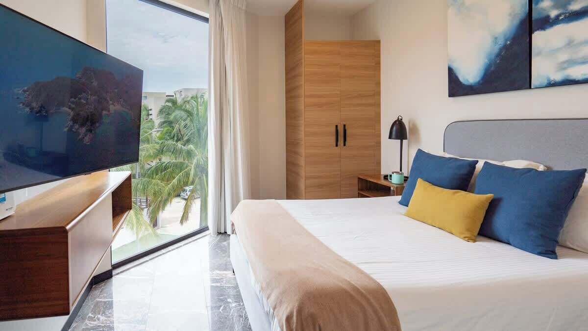 A hotel room with a bed, a TV, a wardrobe, and a view of palm trees.