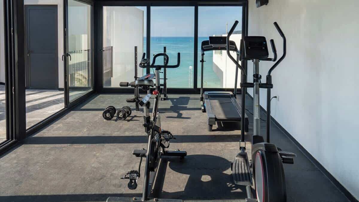 Un gimnasio con equipamiento de ejercicio, una cinta de correr y vistas al océano a través de amplias ventanas.
