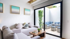 A modern living room with a sofa set, a coffee table, and a large sliding glass door leading to an outdoor seating area. - Chic Studio by 5th Ave with Rooftop Pool and Gym (Playa del Carmen)