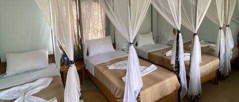 A hotel room with four beds, each with a canopy bedspread and a mosquito net.