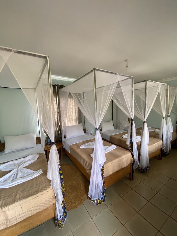 Una habitación de hotel con cuatro camas, cada una con dosel y mosquitero.