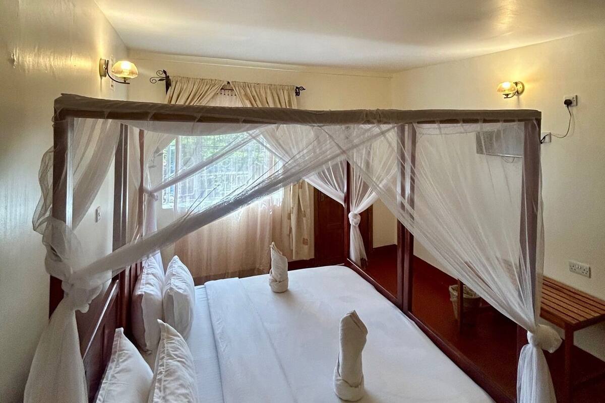 A four-poster bed with a canopy, white linens, and a bedside table with a lamp.