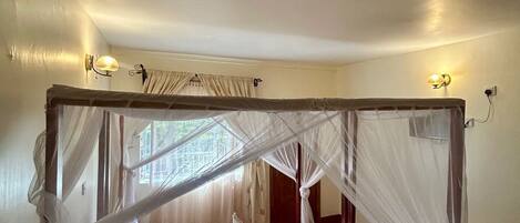 A four-poster bed with a canopy, white linens, and a bedside table with a lamp.