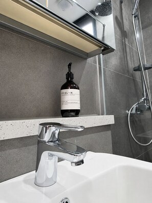 A bathroom with a modern sink, a handheld showerhead, and a bottle of Roslyn hand wash on a countertop. - Somsom House (Seogwipo)