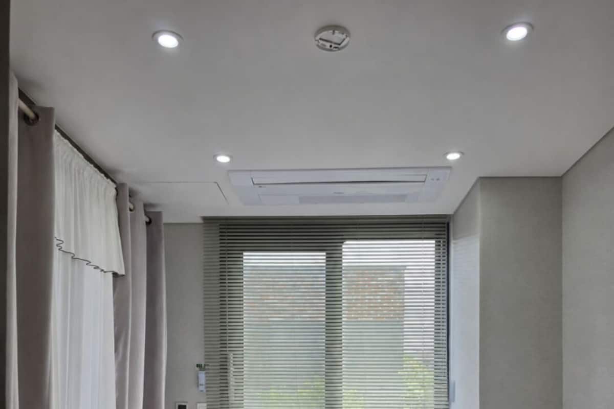 Une chambre Ă coucher avec un lit, une fenĂȘtre avec des stores, une table de chevet avec une lampe et un luminaire au plafond.