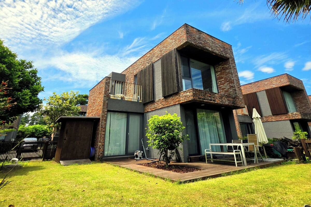 A modern two-story house with a brick facade, large windows, and a well-maintained lawn.