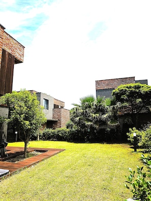 A courtyard with a grassy lawn, a wooden deck, and a brick building with a modern design. - Somsom House (Seogwipo)