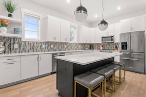 A modern kitchen with white cabinets, a black island with bar stools, stainless steel appliances, and a mosaic backsplash. - BF ~ 5 Beds w/ Elevator ~ Free Secure Parking ~ West End ~ Near Vanderbilt and Tons of Restaurants (Nashville)