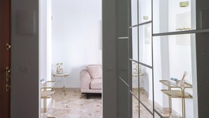 Una habitación con piso de mármol, un sofá rosa, una mesita con un teléfono antiguo y un separador de vidrio con barras de metal.
