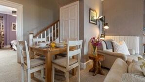 A dining area with a wooden table and chairs, a staircase, and a living room with a sofa and a lamp. - Caldey Island View - Sea Views and Log Burner (Tenby)