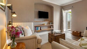 A living room with a beige sofa, a coffee table, a TV mounted on the wall, and a bookshelf with books and decorative items. - Caldey Island View - Sea Views and Log Burner (Tenby)