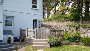 A white building with a wooden fence, steps leading to a door, and a garden with various plants. - Caldey Island View - Sea Views and Log Burner (Tenby)
