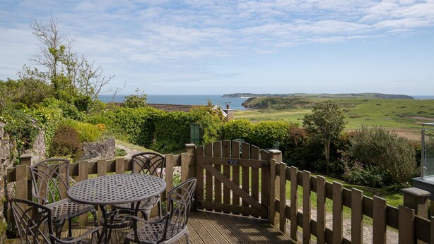 A patio with a table and chairs, overlooking a coastal landscape with a view of the sea and hills. - Caldey Island View - Sea Views and Log Burner (Tenby)
