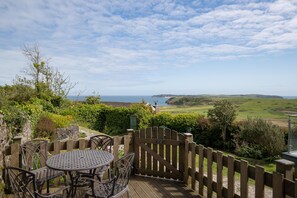 A patio with a table and chairs, overlooking a coastal landscape with a view of the sea and hills. - Caldey Island View - Sea Views and Log Burner (Tenby)