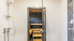 A sauna room with a wooden bench, a shower area with a handheld showerhead, and tiled walls. - Lukupirtti by Interhome (Säkylä)