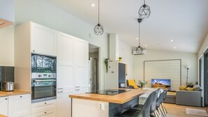 A modern kitchen with white cabinets, a built-in oven, and a wooden island with bar stools. - Lukupirtti by Interhome (Säkylä)