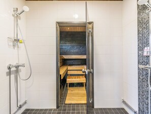 Un espace douche doté d’une porte en verre, d’un banc en bois et d’un mur orné d’un motif en chevrons.