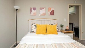 A bedroom with a bed, a bedside table with a lamp, and three wall art pieces. - Cozy Clean Affordable near NDSU and Downtown (Fargo)