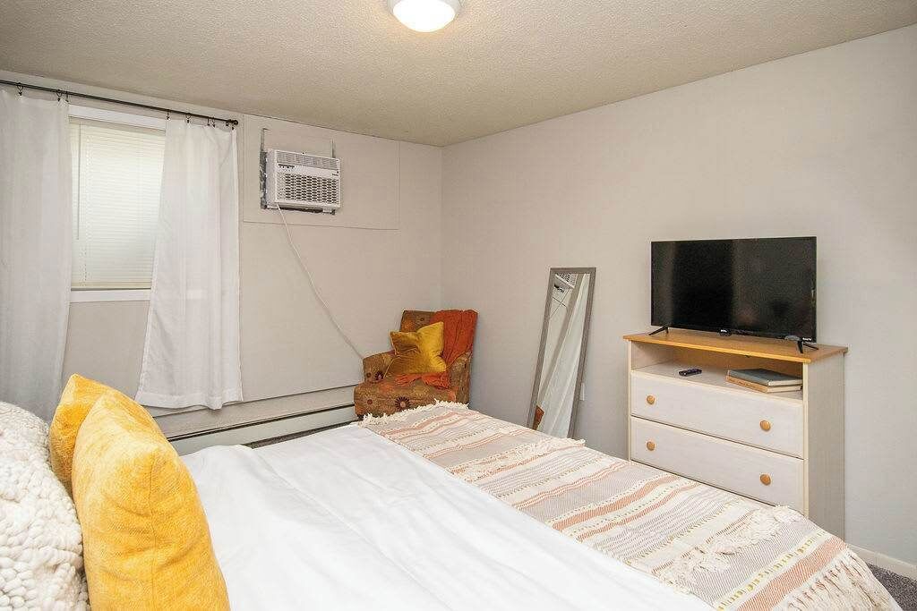 A bedroom with a bed, a television on a dresser, a chair, and a window with curtains.