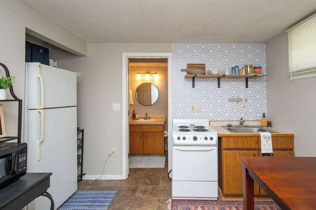 Eine kleine Küche mit Kühlschrank, Herd, Mikrowelle, Holzschränken und einer gemusterten Spritzschutzwand.