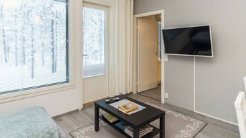 A room with a bed, a coffee table with books, a TV on the wall, and a door leading to another room.