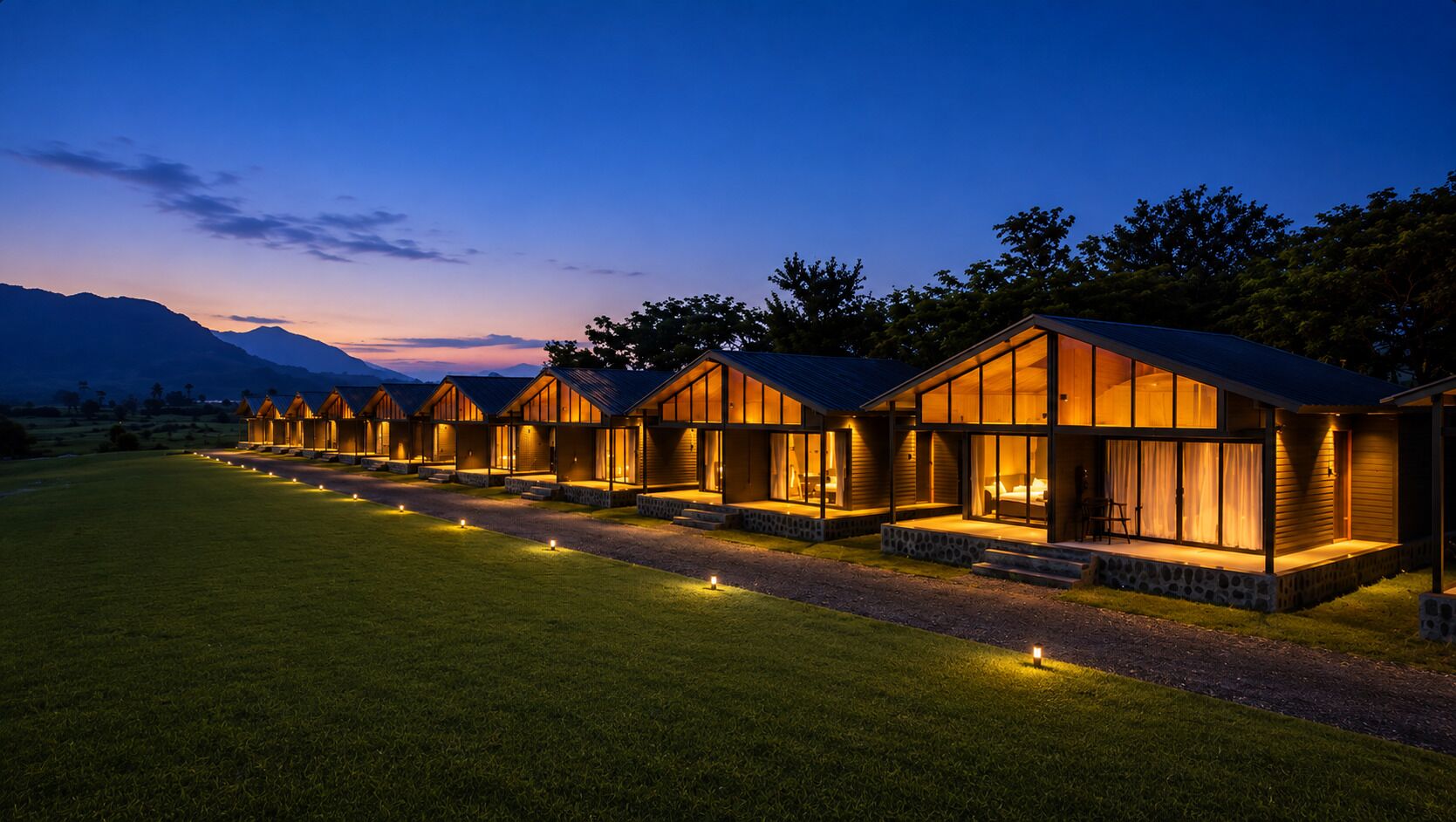 Een rij moderne vakantiehuisjes met grote ramen, een stenen fundering en een goed verlicht pad.
