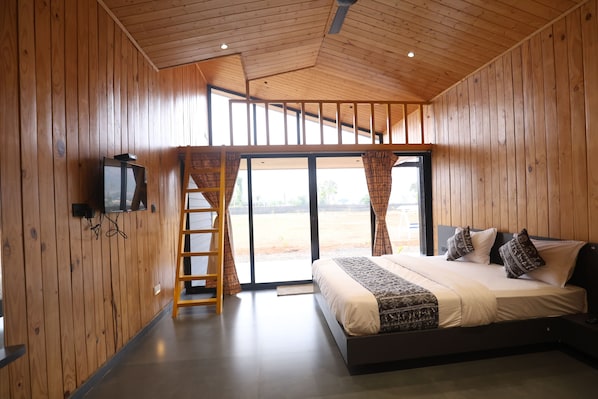 Quarto com painéis de madeira, uma cama, uma televisão e uma escada que dá para uma varanda.