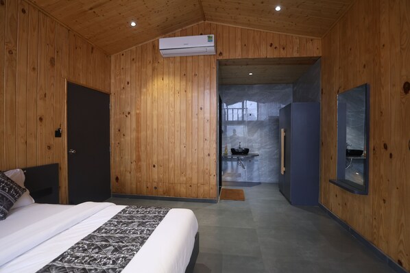Dormitorio con paneles de madera, una cama y un baño visible a través de una puerta abierta, además de un aire acondicionado instalado.