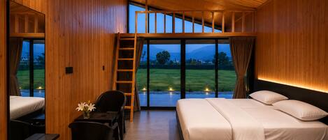 A bedroom with a bed, a desk, and a chair, with a view of a grassy field through large windows.