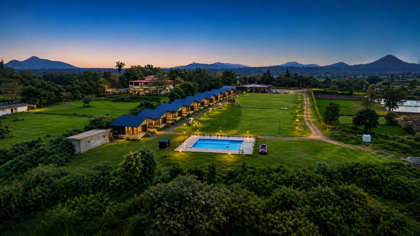 Ein Resort mit mehreren Gästegebäuden, einem Schwimmbad und einer Bergkulisse.