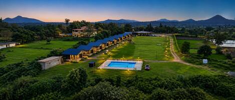 Un resort con varias edificaciones para huéspedes, una piscina y montañas al fondo.