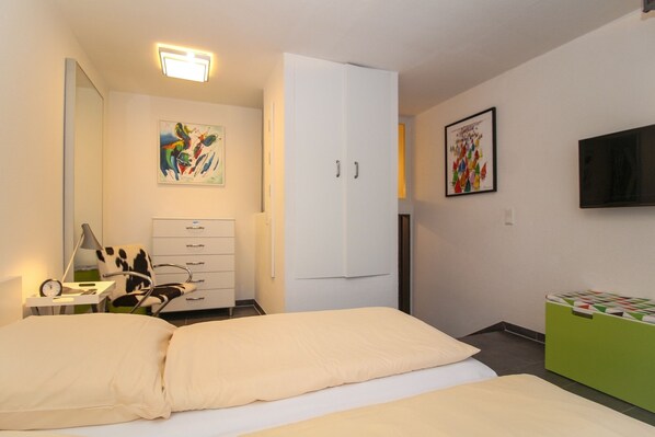 A hotel room with two beds, a desk with a chair, a wardrobe, a mirror, and artwork on the walls.