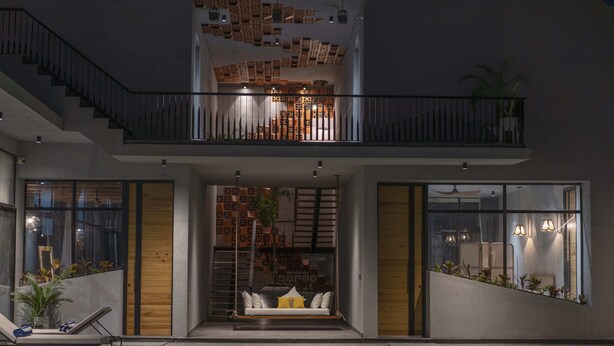 A modern indoor pool area with a lounge chair, a staircase, and a seating area with cushions.