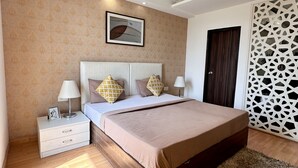 A bedroom with a bed, nightstands, a ceiling fan, a wall-mounted picture, and a patterned wall. - Hotel Flamingo (Gurugram)